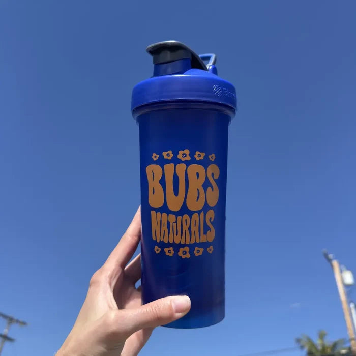 Hand holding a BUBS Naturals Blue Blender Bottle outdoors
