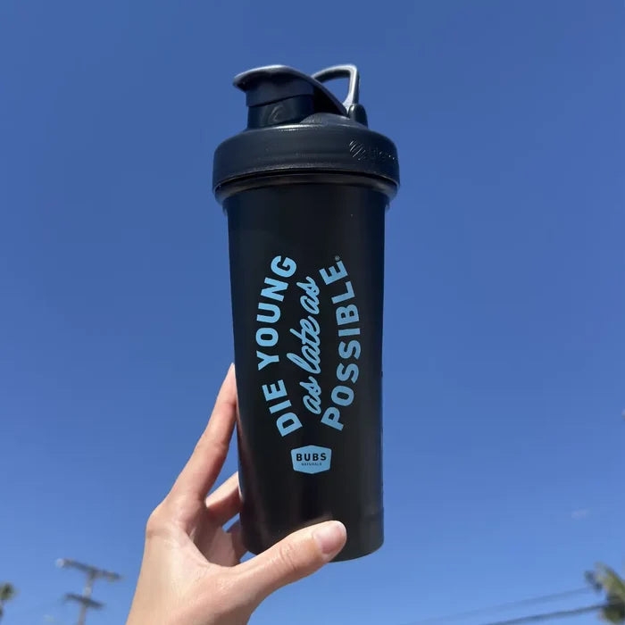 Hand holding a BUBS Naturals Classic Blender Bottle outdoors