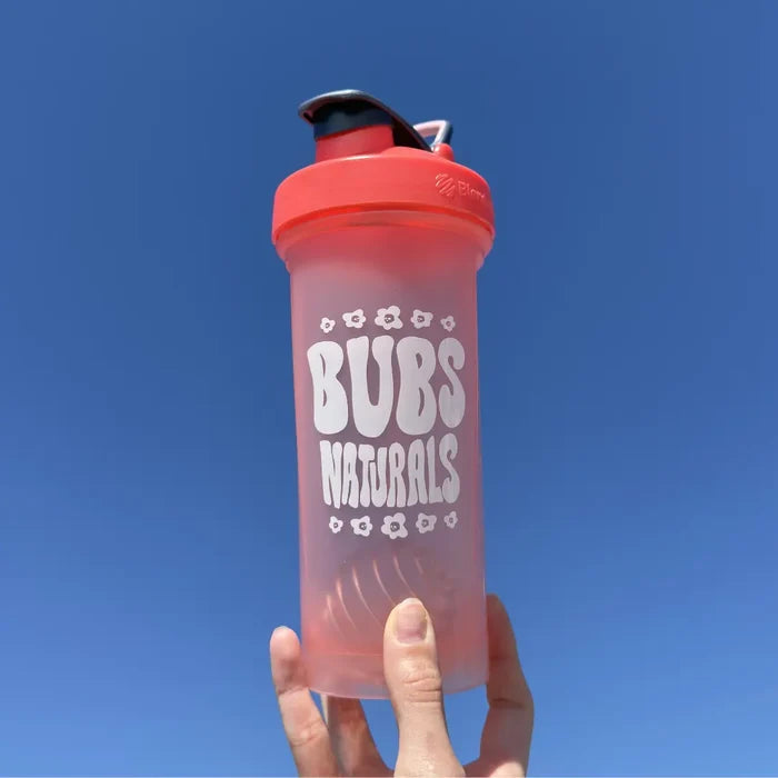 Hand holding a BUBS Naturals Coral Blender Bottle outdoors