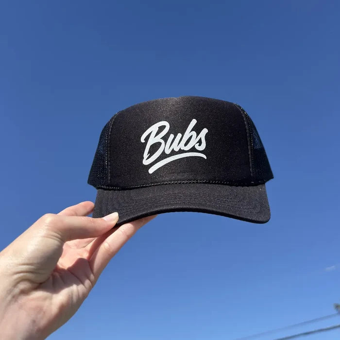 Hand holding a BUBS Black Trucker Hat outdoors