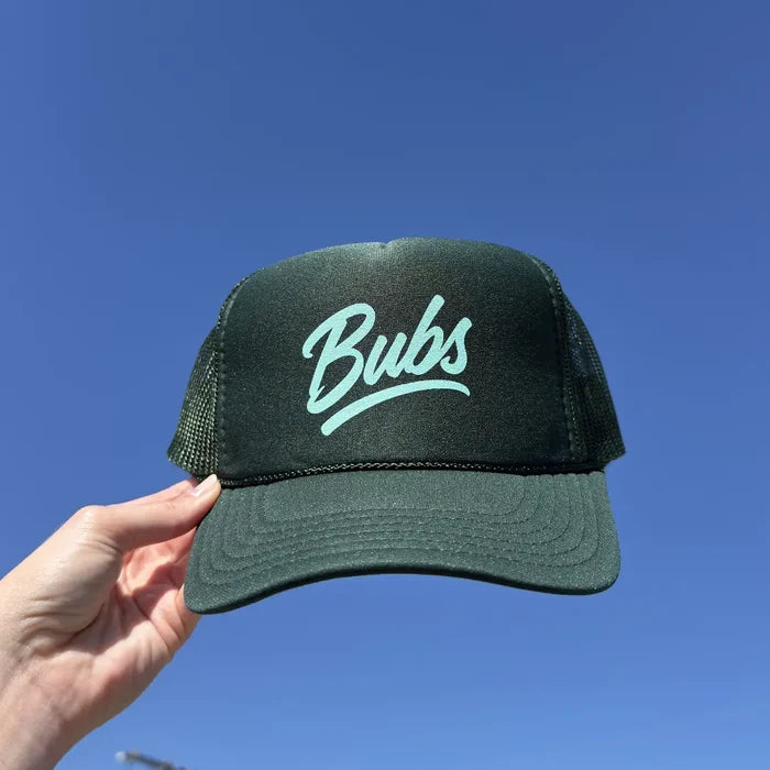Hand holding a BUBS Forest Trucker Hat outdoors