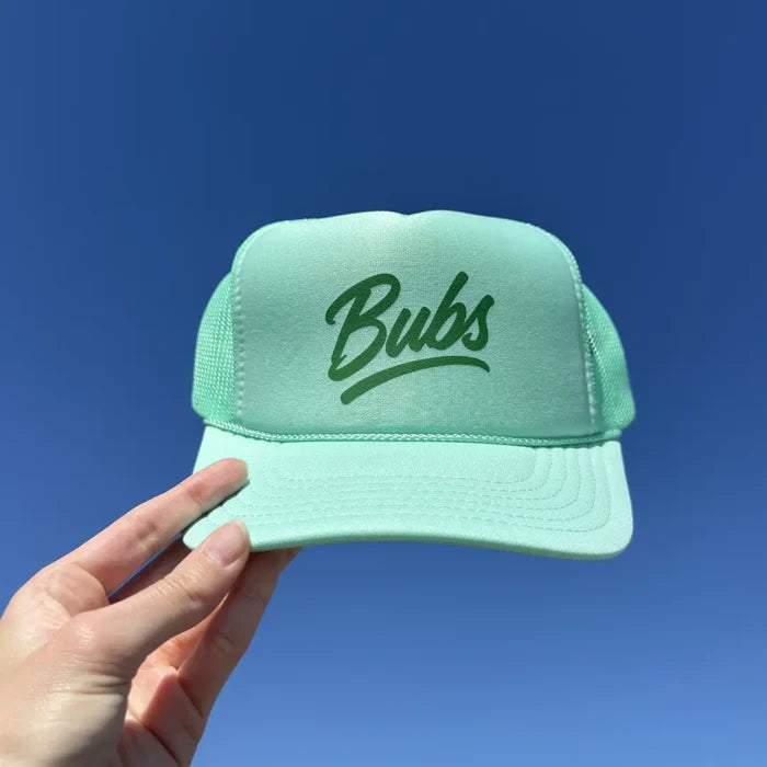 Hand holding a BUBS Seafoam Trucker Hat outdoors