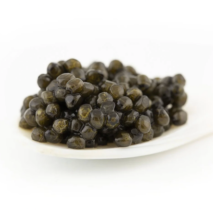 Close-up macro shot of glossy, dark Caviar d'Eden Oscietra pearls delicately served on a traditional white mother-of-pearl spoon