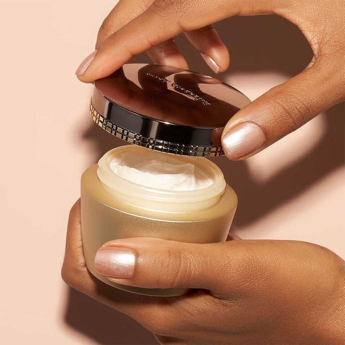 Hand holding a jar of cream with a visible brand name on a beige background